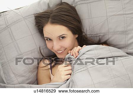 Stock Photo - Portrait of young woman lying in bed. Fotosearch