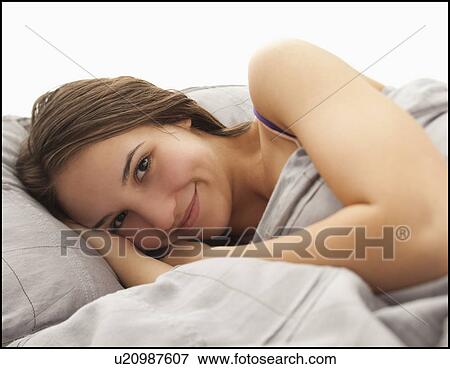 Portrait of young woman lying in bed View Large Photo Image Stock Photo - Portrait of young woman lying in bed. Fotosearch