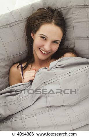 Portrait of young woman lying in bed View Large Photo Image Stock Photograph - Portrait of young woman lying in bed. Fotosearch