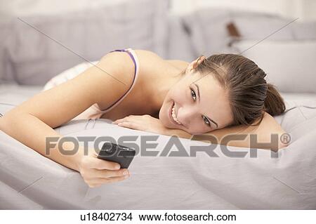 Portrait of young woman using mobile phone on bed View Large Photo Image Picture - Portrait of young woman using mobile phone on bed. Fotosearch