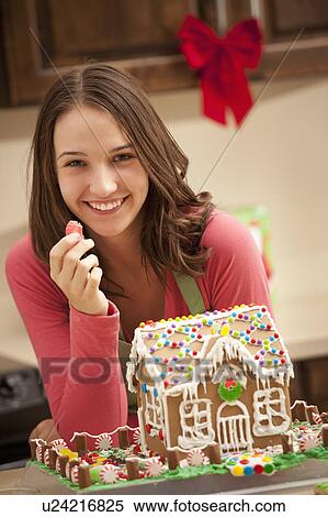Stock Photography - Portrait of young woman with gingerbread house in kitchen. Fotosearch