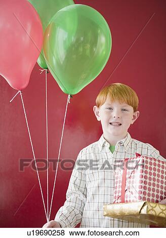 Studio portrait of boy (8-9) holding Christmas gifts and balloons View Large Photo Image Stock Photo - Studio portrait of boy (8-9) holding Christmas gifts and balloons. Fotosearch