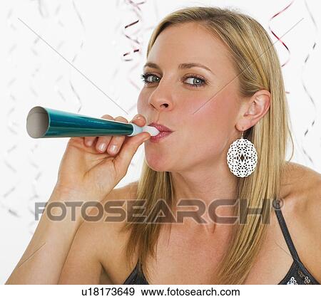 Stock Photo - Studio portrait of young woman blowing party horn. Fotosearch