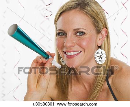 Stock Image - Studio portrait of young woman holding party horn. Fotosearch