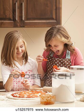 Stock Photography - Two girls (10-11) preparing pizza in kitchen. Fotosearch
