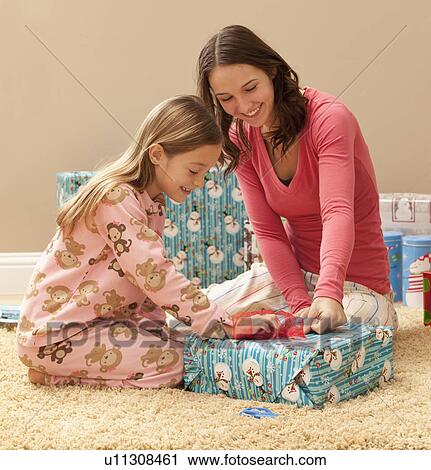 Stock Image - Two sisters (6-7, 18-19) wrapping Christmas presents. Fotosearch