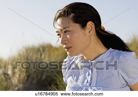 Stock Photography - USA, California, Point Reyes, Young woman sitting in grass on sand dune. Fotosearch