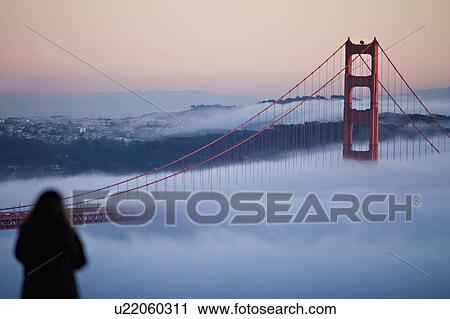 Stock Image - USA, California, San Francisco, Woman watching Golden gate Bridge in fog. Fotosearch