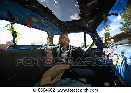 Stock Image - USA, Colorado, Carbondale, Smiling mature woman sitting in vintage car, portrait. Fotosearch