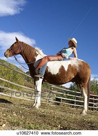 Stock Image - USA, Colorado, Cowgirl relaxing with horse on ranch. Fotosearch