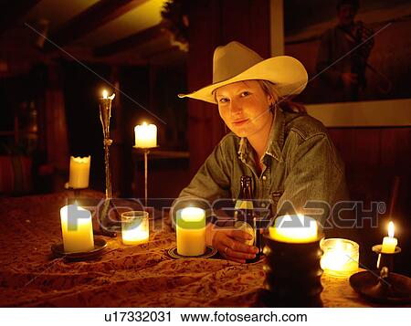 Stock Image - USA, Colorado, Portrait of cowgirl sitting at table with candles. Fotosearch