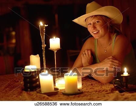 Stock Photograph - USA, Colorado, Portrait of cowgirl sitting at table with candles. Fotosearch