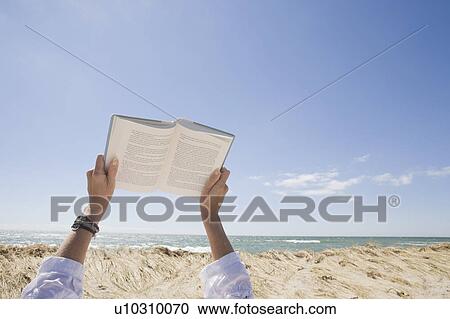 Stock Image - USA, Massachusetts, woman's hands on beach holding book. Fotosearch