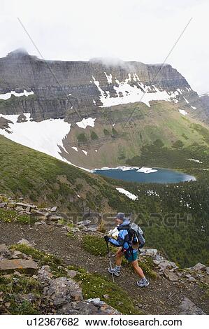 Stock Image - USA, Montana, Glacier National Park, Mid adult woman hiking with backpack during rain. Fotosearch