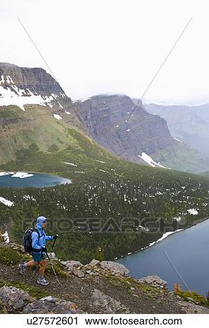Stock Image - USA, Montana, Glacier National Park, Mid adult woman hiking with backpack during rain. Fotosearch