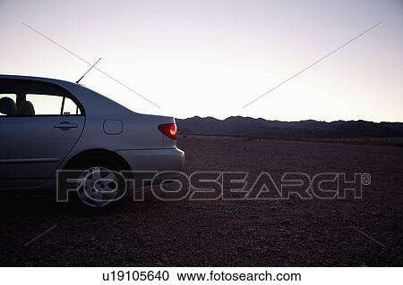 Stock Image - USA, Nevada, car on desert road at dusk. Fotosearch