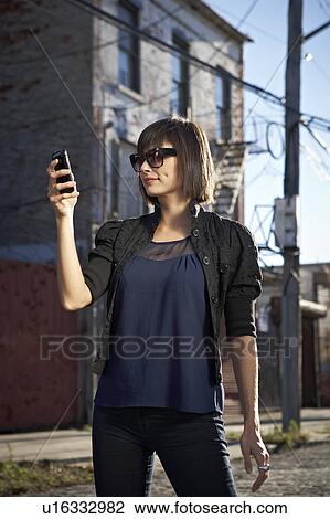 Stock Image - USA, New York City, Brooklyn, woman in street using phone. Fotosearch