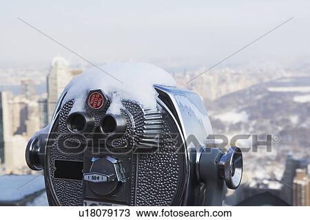 Stock Image - USA, New York City, Coin operated binoculars covered with snow, Central Park in background. Fotosearch