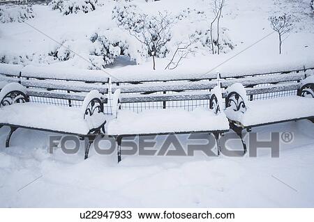 Stock Image - USA, New York City, Manhattan, Benches in Central Park covered with snow. Fotosearch