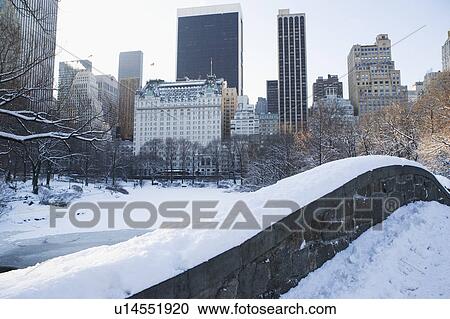 Stock Image - USA, New York City, View of Central Park in winter with Manhattan skyline in background. Fotosearch