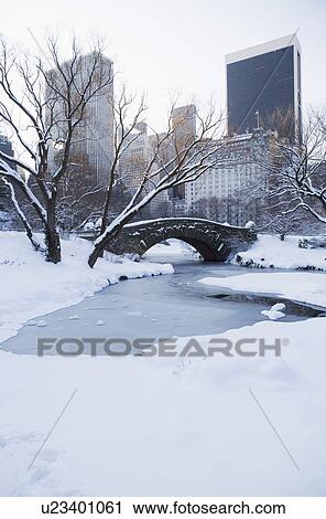 Stock Image - USA, New York City, View of Central Park in winter with Manhattan skyline in background. Fotosearch