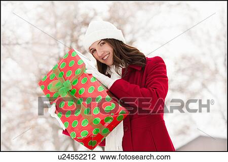 Stock Image - USA, Utah, Lehi, Portrait of young woman holding Christmas gift outdoors. Fotosearch