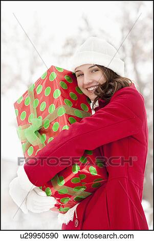 Stock Image - USA, Utah, Lehi, Portrait of young woman hugging Christmas gift outdoors. Fotosearch
