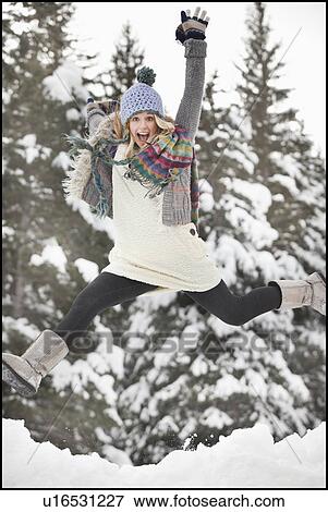 Stock Photo - USA, Utah, Salt Lake City, portrait of young woman in winter clothing leaping. Fotosearch
