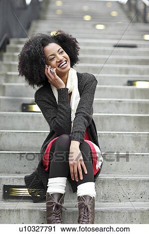 Stock Image - USA, Washington State, Seattle, young woman sitting on steps and talking on mobile phone. Fotosearch