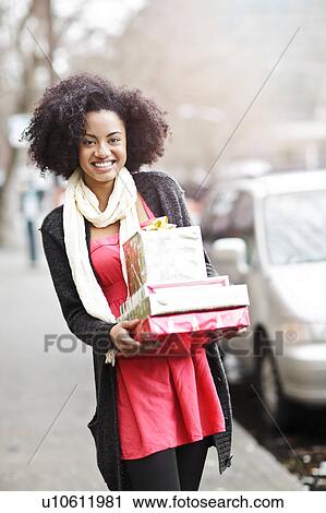 Stock Image - USA, Washington State, Seattle, Young cheerful woman carrying stack of boxed gifts. Fotosearch
