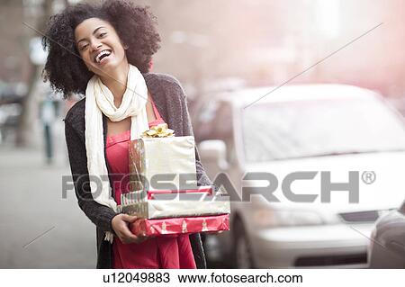 Stock Image - USA, Washington State, Seattle, Young cheerful woman carrying stack of boxed gifts. Fotosearch