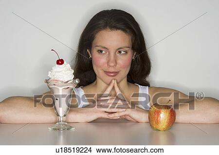 Picture - Woman choosing between ice cream and apple. Fotosearch