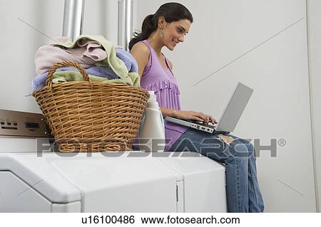 Woman doing laundry and using laptop View Large Photo Image Stock Photograph - Woman doing laundry and using laptop. Fotosearch