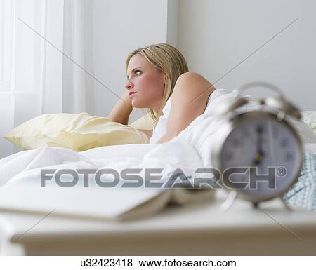Stock Photo - Woman in bed with alarm clock in foreground. Fotosearch