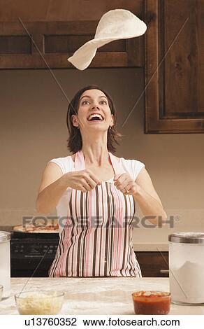 Stock Image - Woman tossing dough in kitchen. Fotosearch
