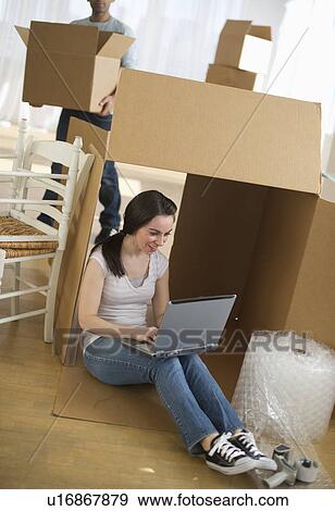 Stock Photo - Woman using laptop by cardboard box. Fotosearch