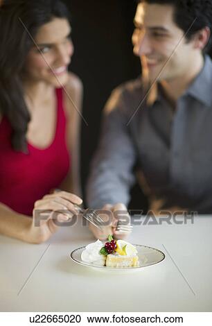 Stock Image - Young happy couple sharing dessert, studio shot. Fotosearch