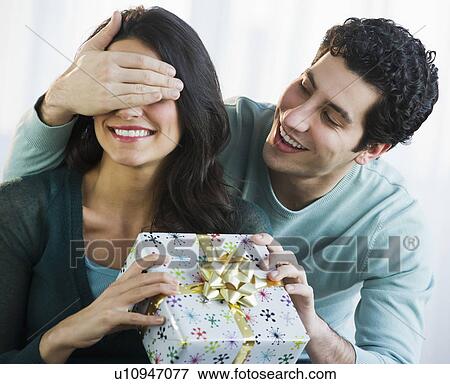 Picture Of Young Man Giving His Friend Present While Covering Picture Young Man Giving His Friend Present While Covering Her Eyes Fotosearch Search