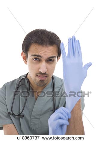 Stock Photo - Young surgeon putting on protective gloves. Fotosearch