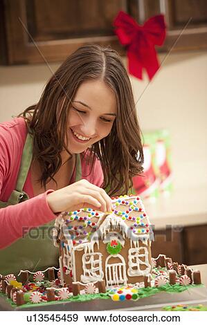 Stock Photo - Young woman decorating gingerbread house in kitchen. Fotosearch