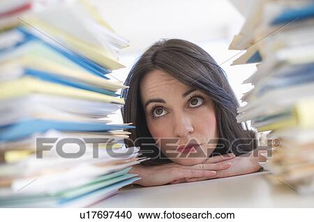 Stock Image - Young woman looking at stack of documents at desk. Fotosearch