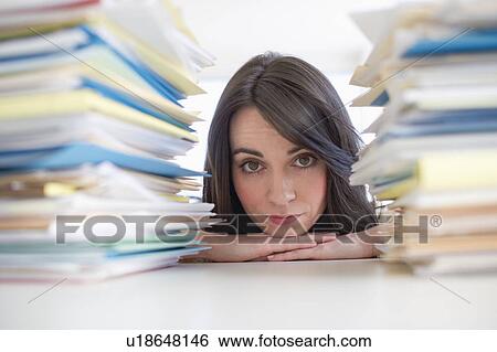 Stock Photograph - Young woman looking at stack of documents at desk. Fotosearch