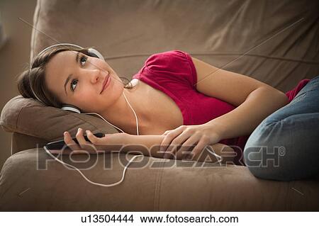 Picture - Young woman lying down on sofa and listening music . Fotosearch
