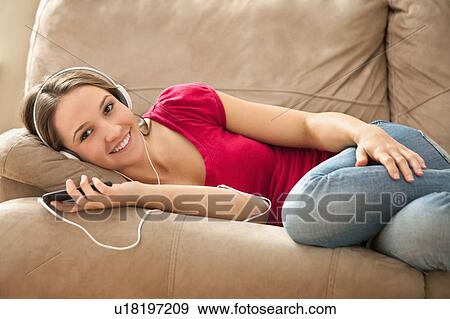 Stock Photo - Young woman lying down on sofa and listening music . Fotosearch