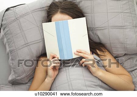 Stock Image - Young woman reading in bed. Fotosearch