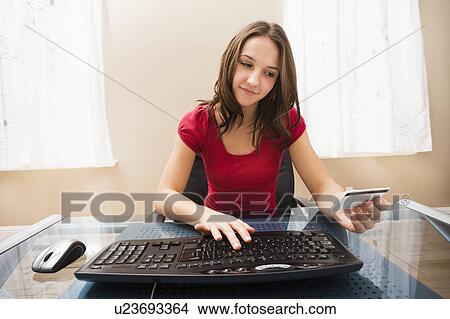 Picture - Young woman using computer and holding credit card. Fotosearch