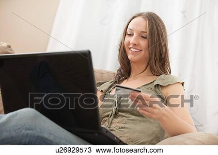 Stock Image - Young woman using laptop and holding credit card. Fotosearch