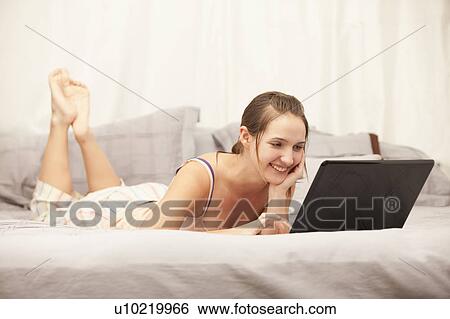 Young woman using laptop on bed View Large Photo Image Stock Photograph - Young woman using laptop on bed. Fotosearch