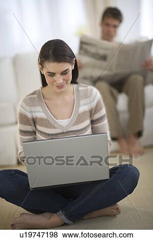 Young woman using laptop while man is reading newspaper in background View Large Photo Image Stock Photo - Young woman using laptop while man is reading newspaper in background. Fotosearch