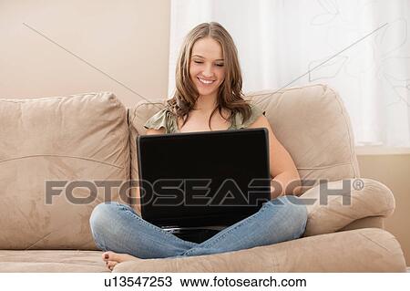Young woman using laptop while sitting at sofa View Large Photo Image Stock Image - Young woman using laptop while sitting at sofa. Fotosearch